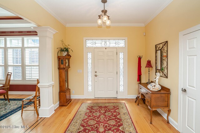 foyer with a notable chandelier, baseboards, light wood-type flooring, ornate columns, and crown molding