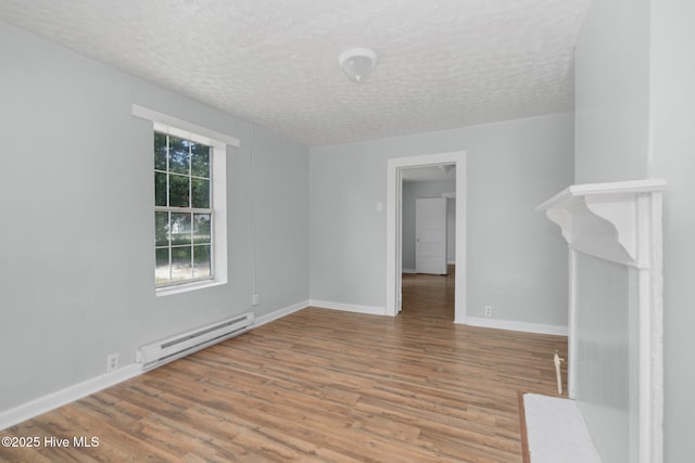 empty room featuring a baseboard heating unit, a textured ceiling, baseboards, and wood finished floors