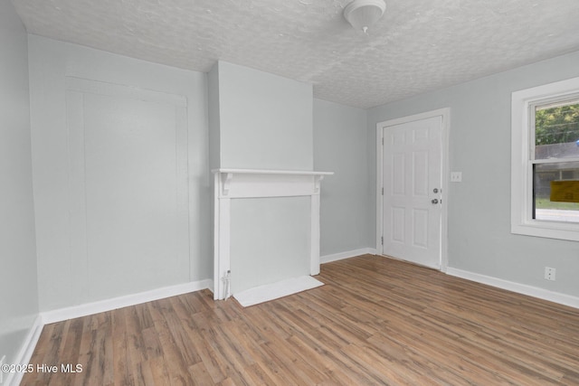 unfurnished living room with a textured ceiling, baseboards, and wood finished floors