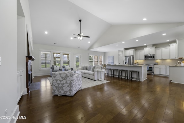 living area featuring a fireplace with flush hearth, ceiling fan, dark wood-type flooring, high vaulted ceiling, and recessed lighting