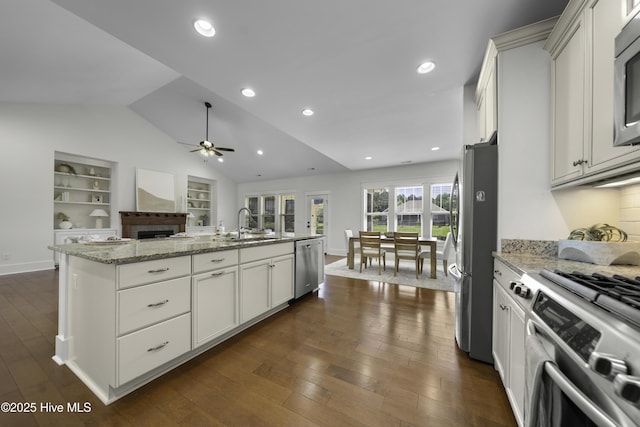 kitchen featuring lofted ceiling, light stone counters, stainless steel appliances, dark wood-style floors, and a center island with sink