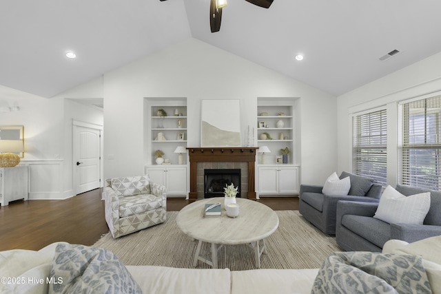 living area featuring built in features, lofted ceiling, visible vents, wood finished floors, and a tile fireplace