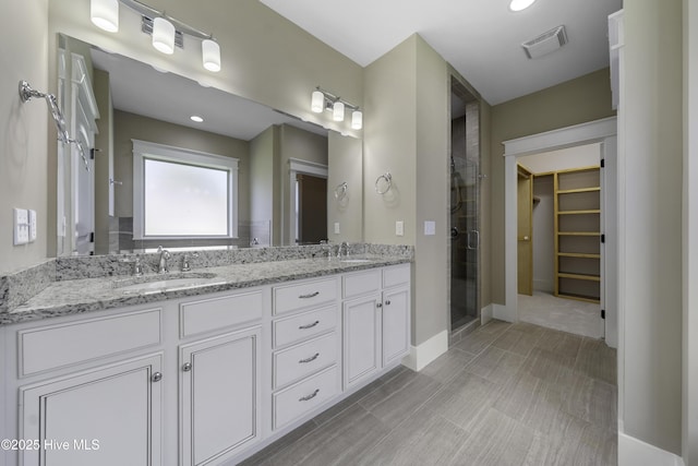 full bathroom featuring double vanity, a stall shower, visible vents, a walk in closet, and a sink