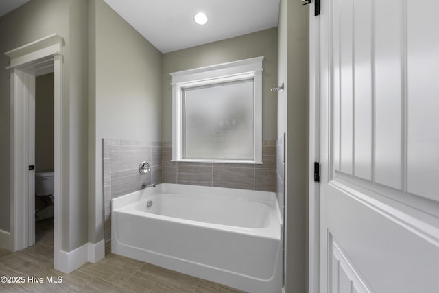 full bathroom featuring toilet, baseboards, and a bath