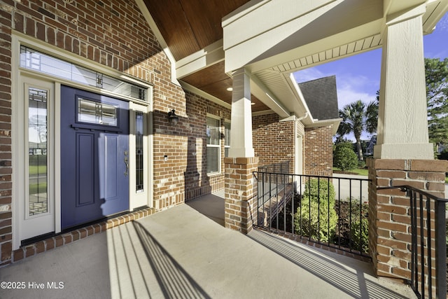 view of exterior entry featuring covered porch and brick siding