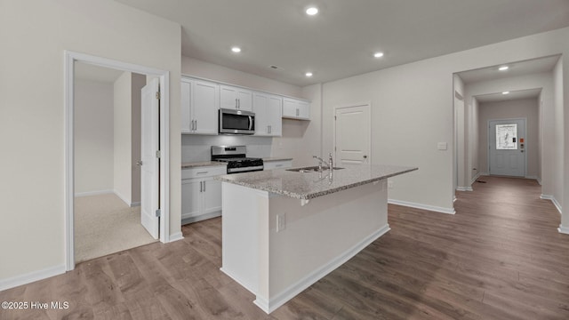 kitchen with white cabinets, wood finished floors, a kitchen island with sink, stainless steel appliances, and a sink