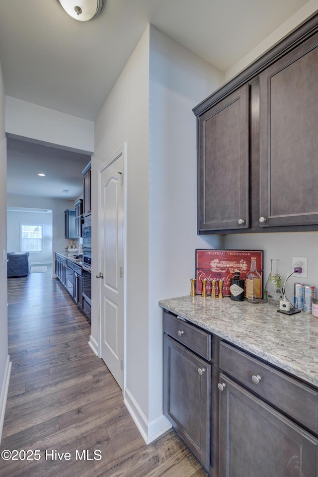 kitchen with dark brown cabinetry, stainless steel oven, wood finished floors, and baseboards