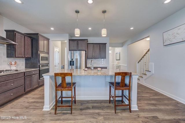 kitchen featuring a breakfast bar, wood finished floors, stainless steel appliances, light stone countertops, and dark brown cabinets