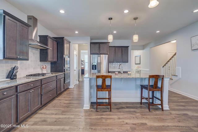 kitchen with wall chimney range hood, dark brown cabinets, wood finished floors, and stainless steel appliances