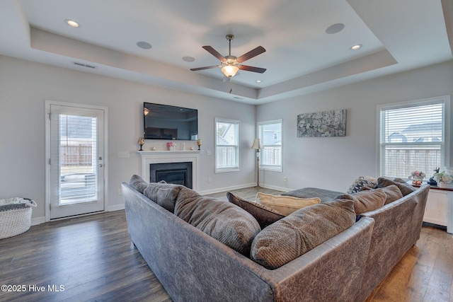 living area featuring visible vents, hardwood / wood-style flooring, a glass covered fireplace, baseboards, and a raised ceiling