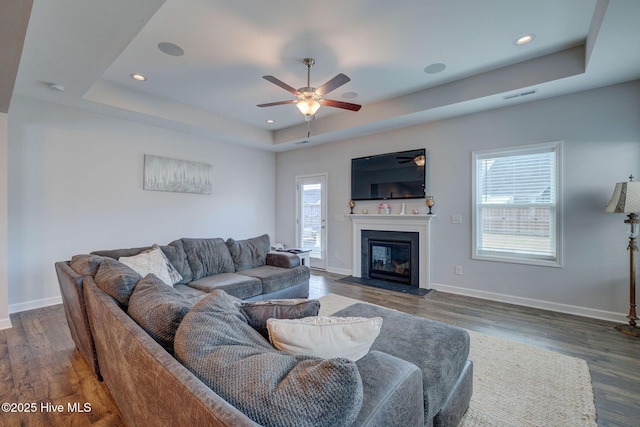 living area with a tray ceiling, dark wood-style floors, baseboards, and visible vents