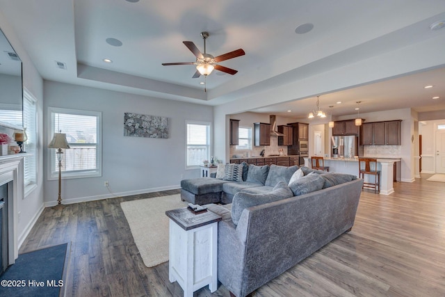 living room with visible vents, a glass covered fireplace, wood finished floors, baseboards, and a raised ceiling