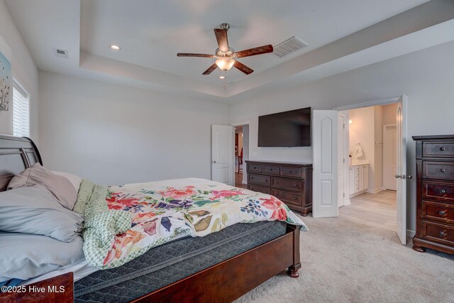 bedroom featuring ceiling fan, a tray ceiling, visible vents, and light carpet