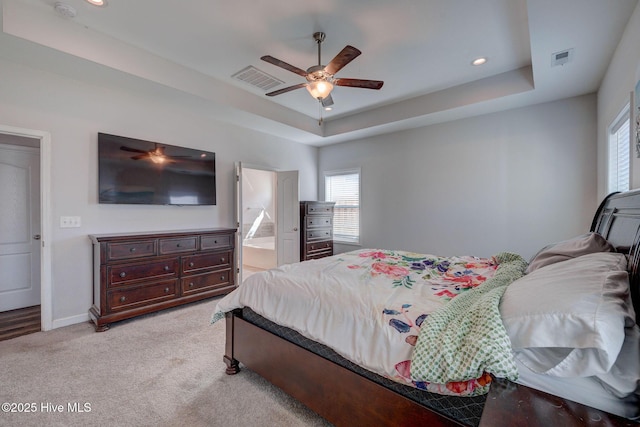 bedroom with a tray ceiling, light colored carpet, and visible vents