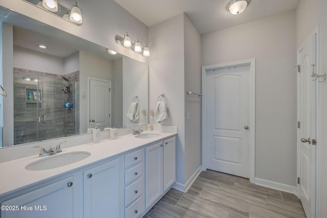 bathroom featuring a sink, baseboards, a stall shower, and double vanity