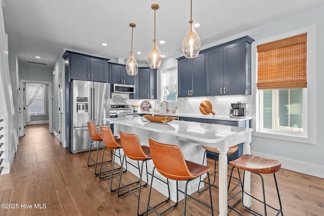 kitchen featuring a breakfast bar area, light countertops, wood finished floors, stainless steel appliances, and a sink