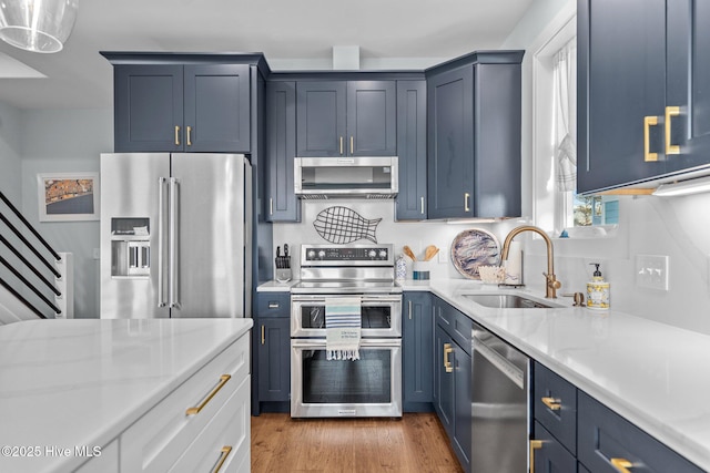 kitchen with blue cabinetry, light stone counters, appliances with stainless steel finishes, wood finished floors, and a sink