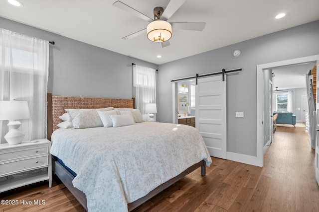 bedroom featuring baseboards, a barn door, recessed lighting, hardwood / wood-style flooring, and ensuite bath