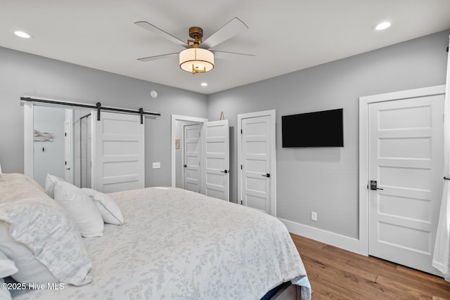 bedroom with wood finished floors, baseboards, recessed lighting, ceiling fan, and a barn door