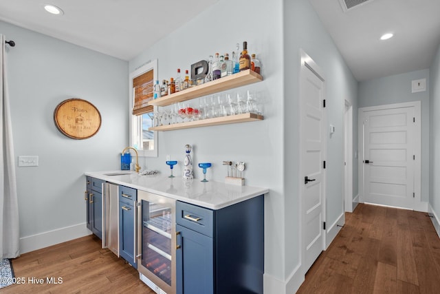 bar featuring beverage cooler, a sink, wood finished floors, wet bar, and baseboards