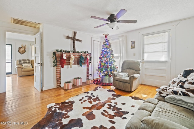 living area featuring ceiling fan, a textured ceiling, visible vents, and wood finished floors