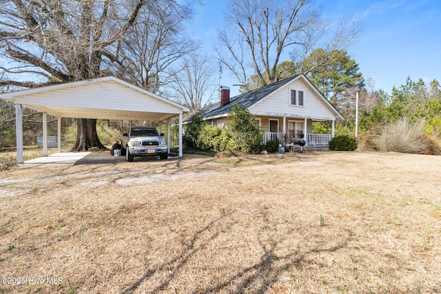 view of front of home with a porch, dirt driveway, a carport, a front lawn, and a chimney