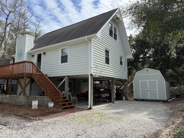 back of property with a shingled roof, a patio area, stairs, a storage shed, and an outbuilding