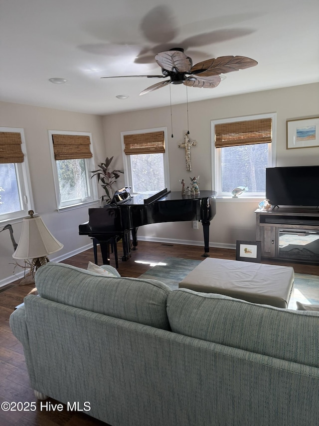 living area with a ceiling fan, baseboards, and dark wood-type flooring