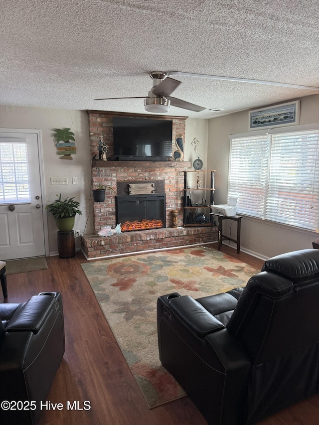 living area with a brick fireplace, ceiling fan, a textured ceiling, wood finished floors, and baseboards