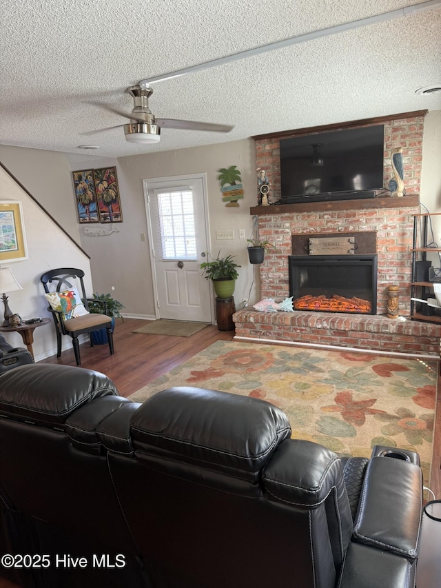 living room featuring a fireplace, a ceiling fan, a textured ceiling, wood finished floors, and baseboards