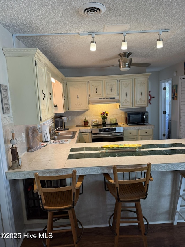 kitchen featuring stainless steel electric range oven, tile counters, visible vents, black microwave, and under cabinet range hood