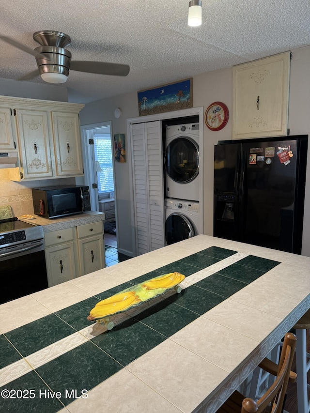 kitchen featuring stacked washer and dryer, a ceiling fan, extractor fan, a textured ceiling, and black appliances