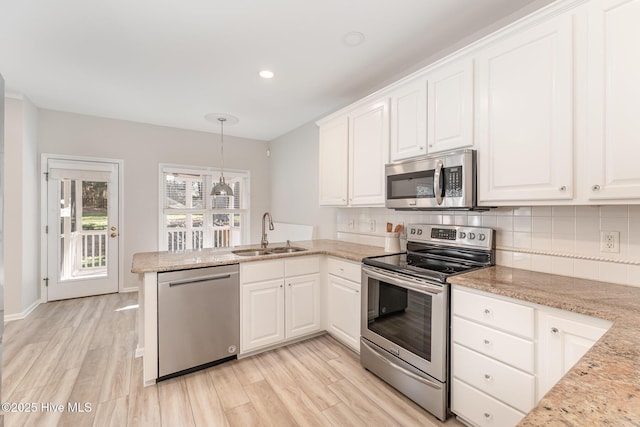 kitchen with decorative backsplash, a peninsula, stainless steel appliances, white cabinetry, and a sink