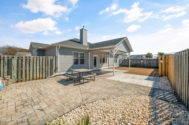 back of house featuring a patio area, a fenced backyard, a chimney, and a shingled roof