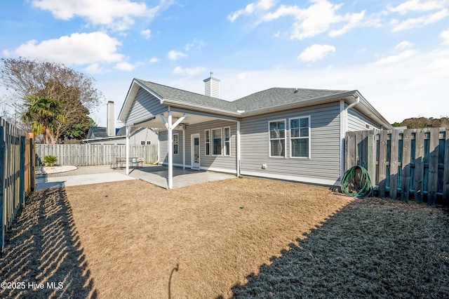 rear view of property with a fenced backyard, a yard, roof with shingles, a chimney, and a patio area