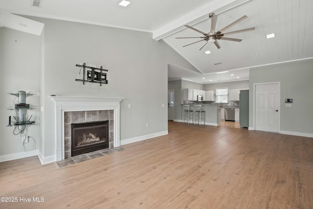 unfurnished living room with vaulted ceiling with beams, light wood finished floors, a ceiling fan, a tile fireplace, and baseboards