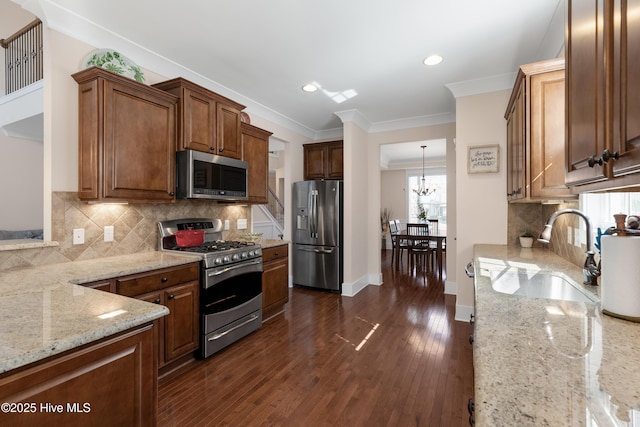 kitchen featuring a chandelier, appliances with stainless steel finishes, ornamental molding, light stone countertops, and dark wood-style floors