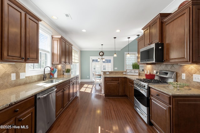 kitchen featuring appliances with stainless steel finishes, dark wood-type flooring, a sink, a chandelier, and a peninsula