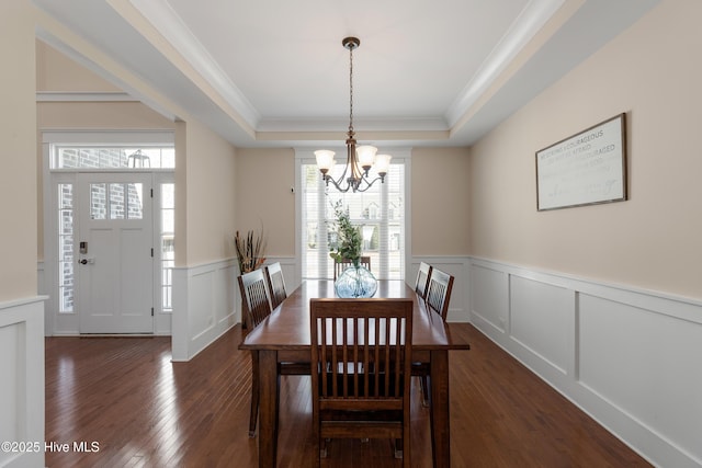 dining area with a decorative wall, a notable chandelier, a tray ceiling, dark wood finished floors, and crown molding