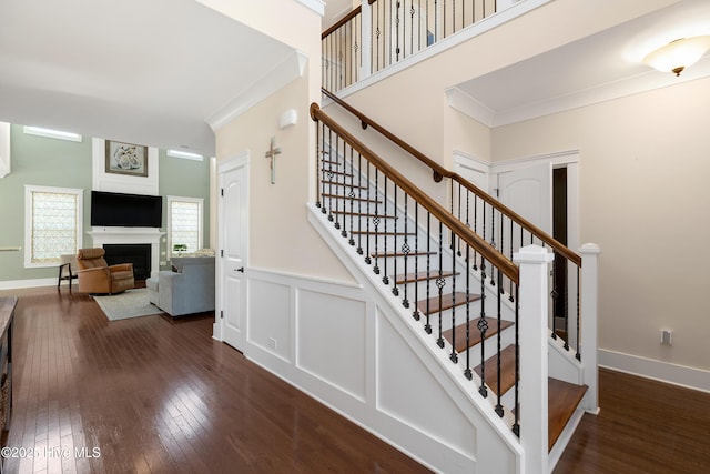 stairs with a decorative wall, a wainscoted wall, a fireplace, hardwood / wood-style floors, and crown molding