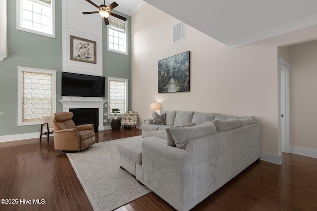 living area featuring a large fireplace, baseboards, visible vents, dark wood finished floors, and a towering ceiling