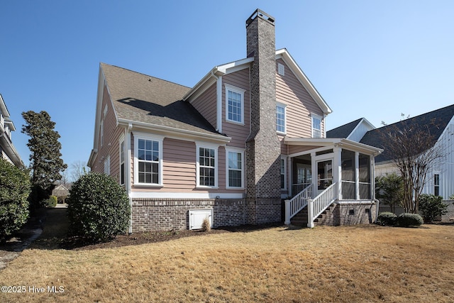 view of side of home with a lawn, a sunroom, a chimney, roof with shingles, and brick siding