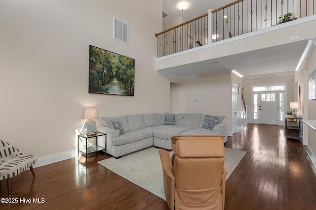 living room featuring visible vents, hardwood / wood-style floors, a high ceiling, ornamental molding, and baseboards