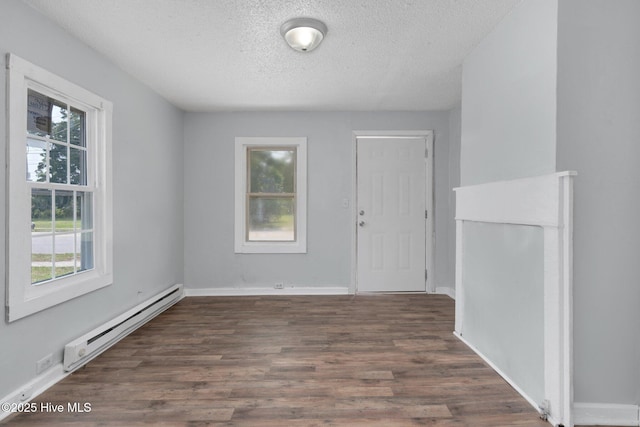 spare room featuring a textured ceiling, baseboards, baseboard heating, and wood finished floors