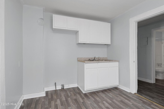 kitchen featuring baseboards, white cabinetry, dark wood-type flooring, and a sink