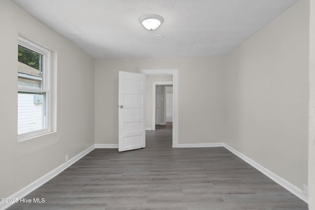 unfurnished room with a healthy amount of sunlight, a textured ceiling, baseboards, and wood finished floors