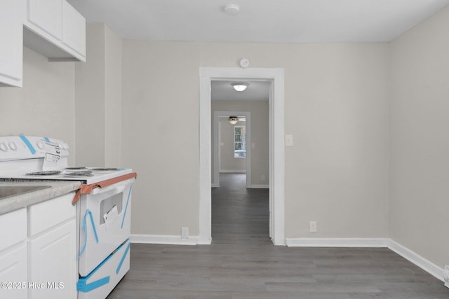 kitchen with electric stove, white cabinetry, baseboards, and wood finished floors