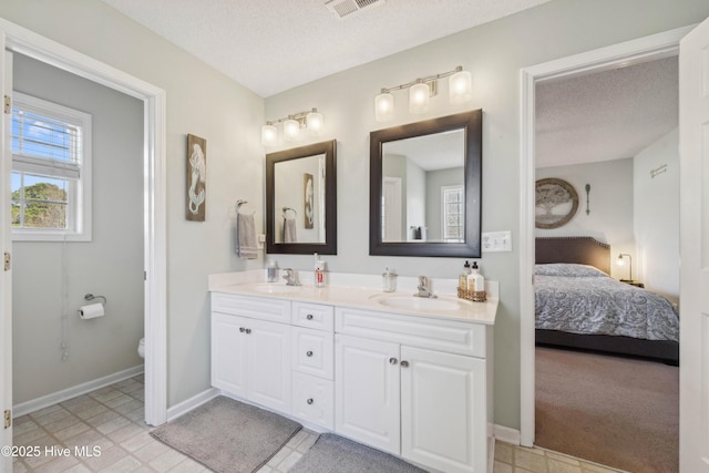 ensuite bathroom featuring a textured ceiling, double vanity, connected bathroom, and a sink