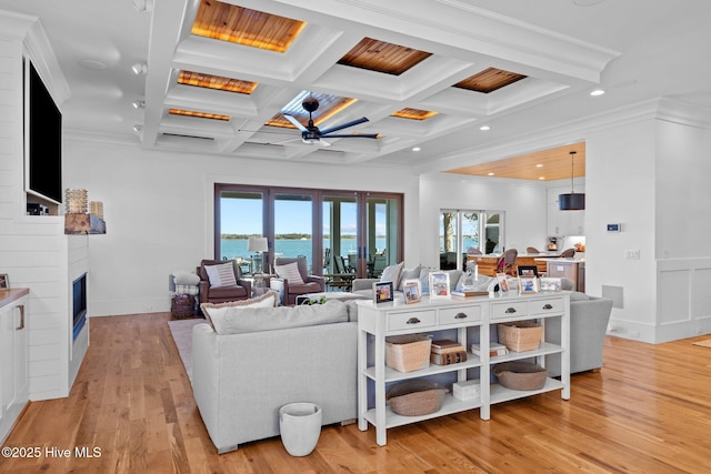 living area with a healthy amount of sunlight, a large fireplace, light wood-style flooring, and coffered ceiling