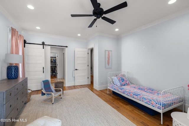 bedroom featuring recessed lighting, wood finished floors, crown molding, and a barn door